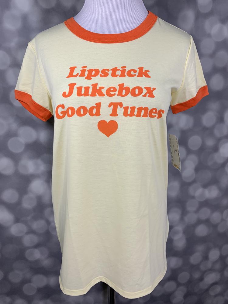 LuLaRoe Liv Tee ivory shirt with orange lipstick jukebox good tunes graphic and ringer trim on a mannequin against a blurred background