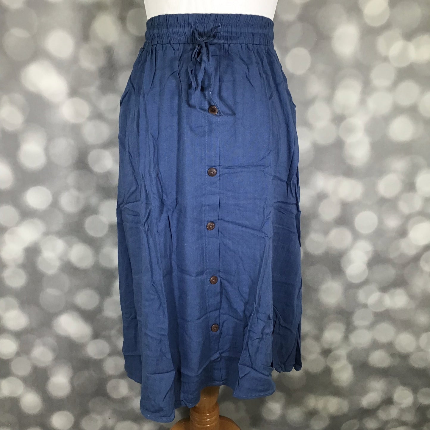 LuLaRoe Marsha skirt in solid coastal denim blue with elastic drawstring waistband, front button placket, and midi-length flowy silhouette on mannequin against a blurred background