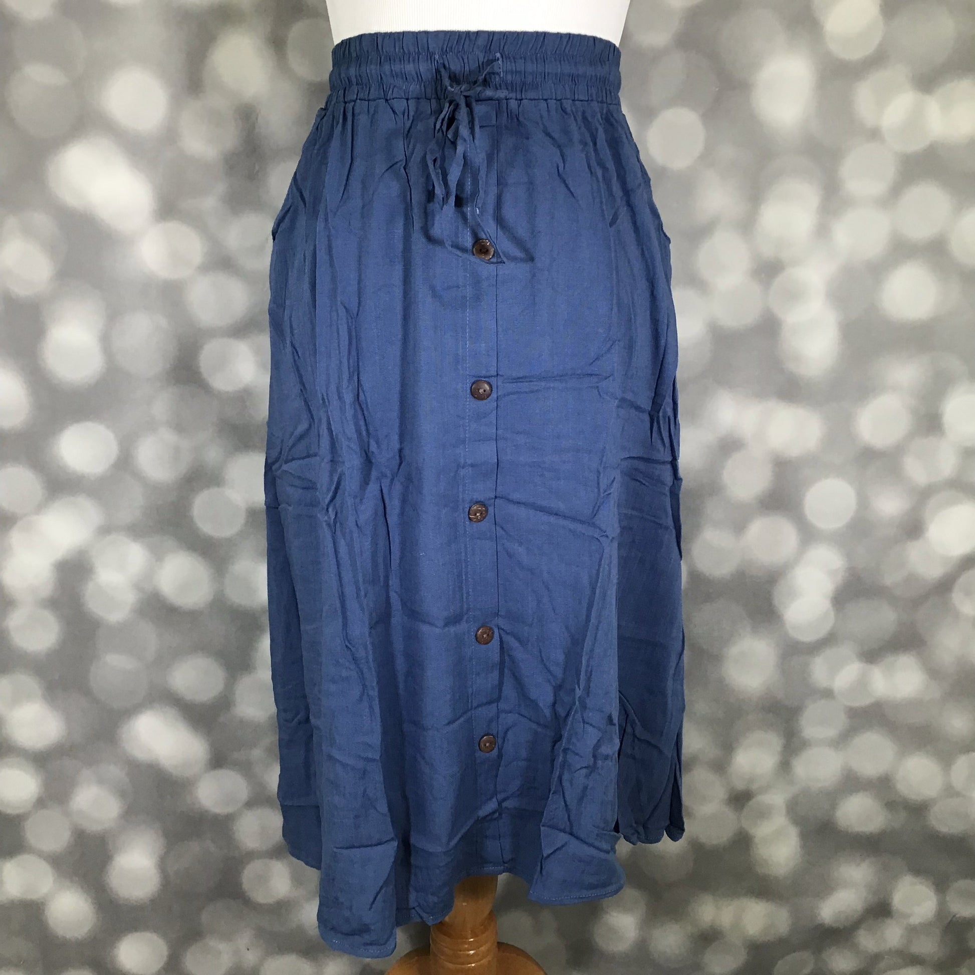 LuLaRoe Marsha skirt in solid coastal denim blue with elastic drawstring waistband, front button placket, and midi-length flowy silhouette on mannequin against a blurred background