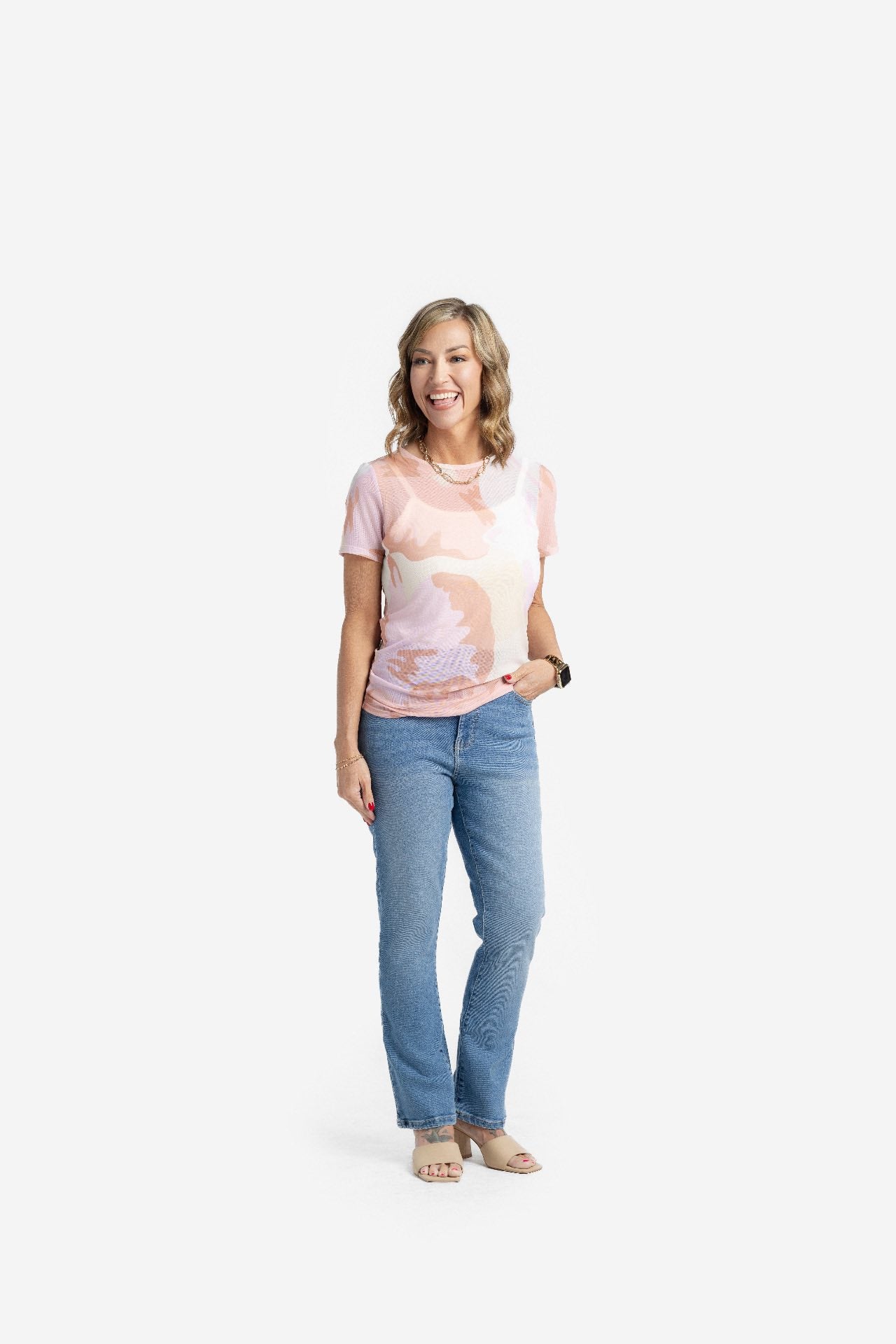 Woman wearing a LuLaRoe Miranda Mesh T featuring blush pink, nude, ivory, and soft peach abstract watercolor prints paired with light wash denim jeans in a neutral minimalist boutique fashion style.