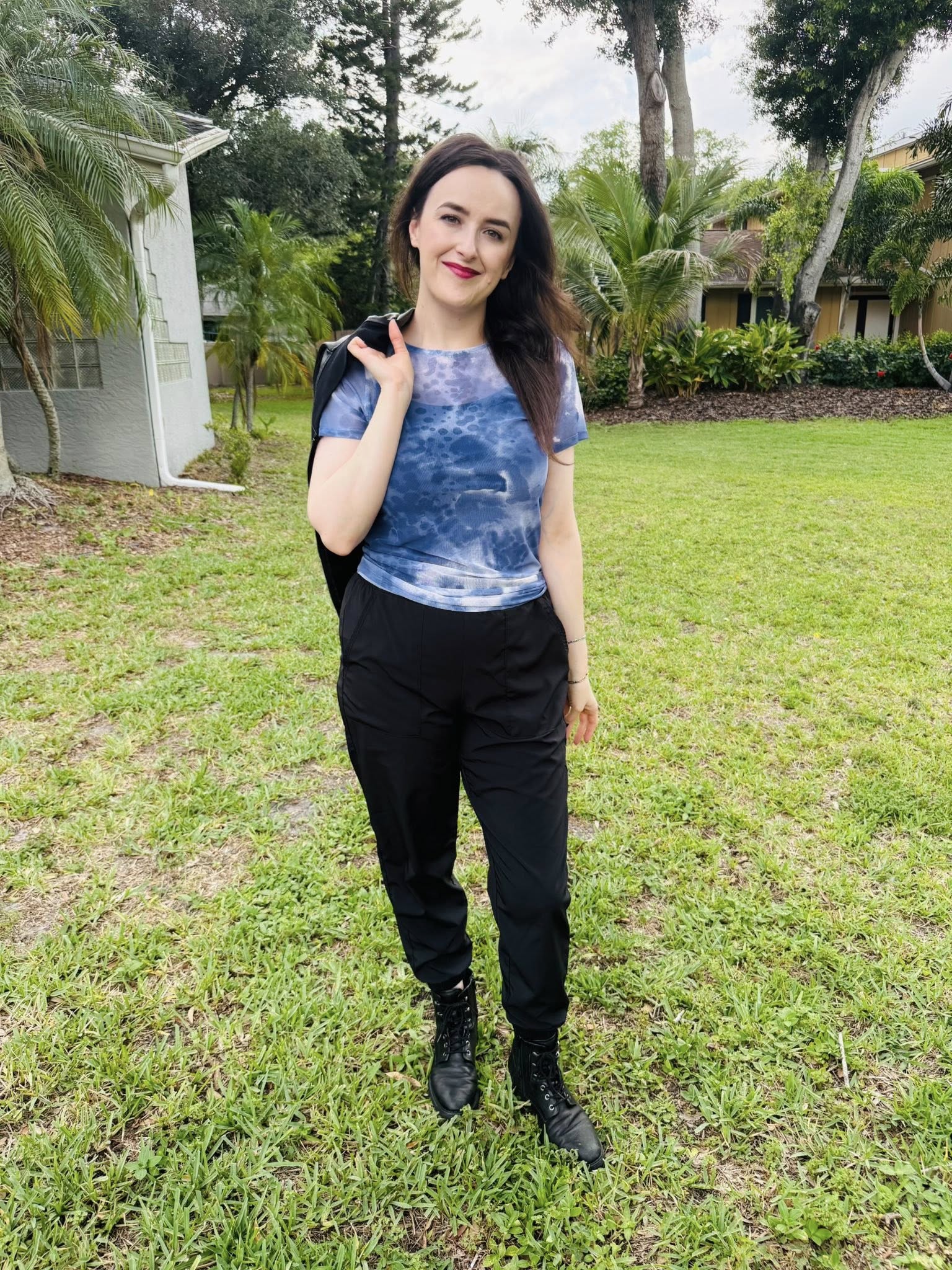 Woman wearing a LuLaRoe Miranda Mesh T featuring deep indigo blue watercolor abstract prints paired with black joggers and combat boots in an edgy casual boutique fashion look  standing outdoors on grass with trees in the background