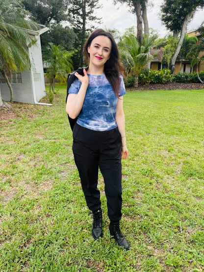 Woman wearing a LuLaRoe Miranda Mesh T featuring deep indigo blue watercolor abstract prints paired with black joggers and combat boots in an edgy casual boutique fashion look  standing outdoors on grass with trees in the background