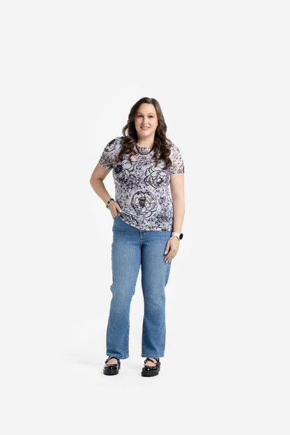 Woman wearing a LuLaRoe Miranda Mesh T featuring black floral sketch prints and abstract splatter details on an ivory background paired with blue denim jeans in a chic monochrome boutique fashion look.