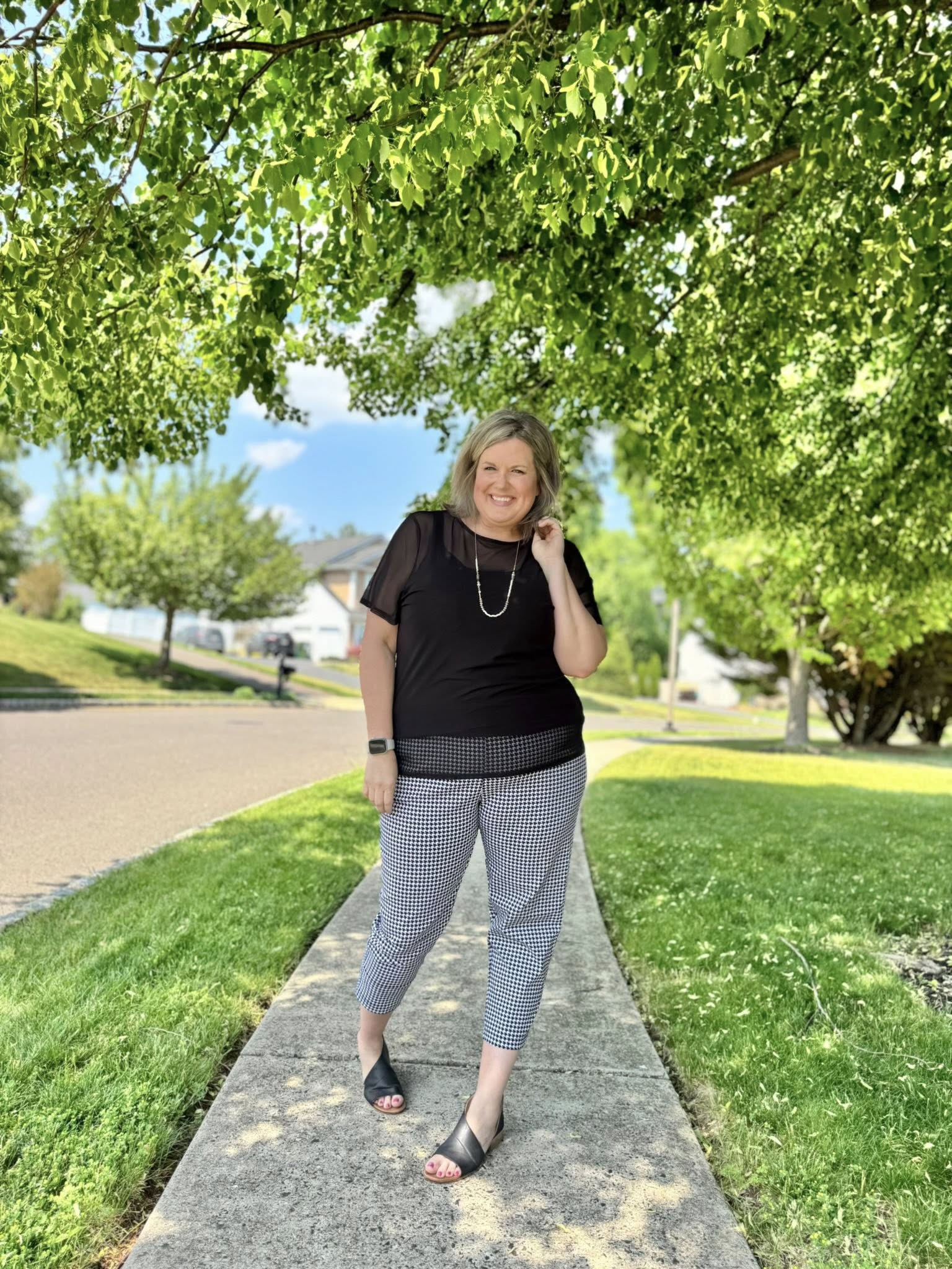 Woman wearing a solid black LuLaRoe Miranda Mesh T semi-sheer mesh layering top paired with black and white patterned ankle pants outdoors in a chic minimalist boutique fashion look.