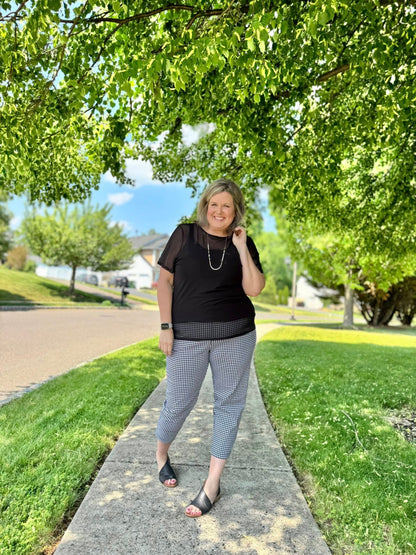Woman wearing a solid black LuLaRoe Miranda Mesh T semi-sheer mesh layering top paired with black and white patterned ankle pants outdoors in a chic minimalist boutique fashion look.