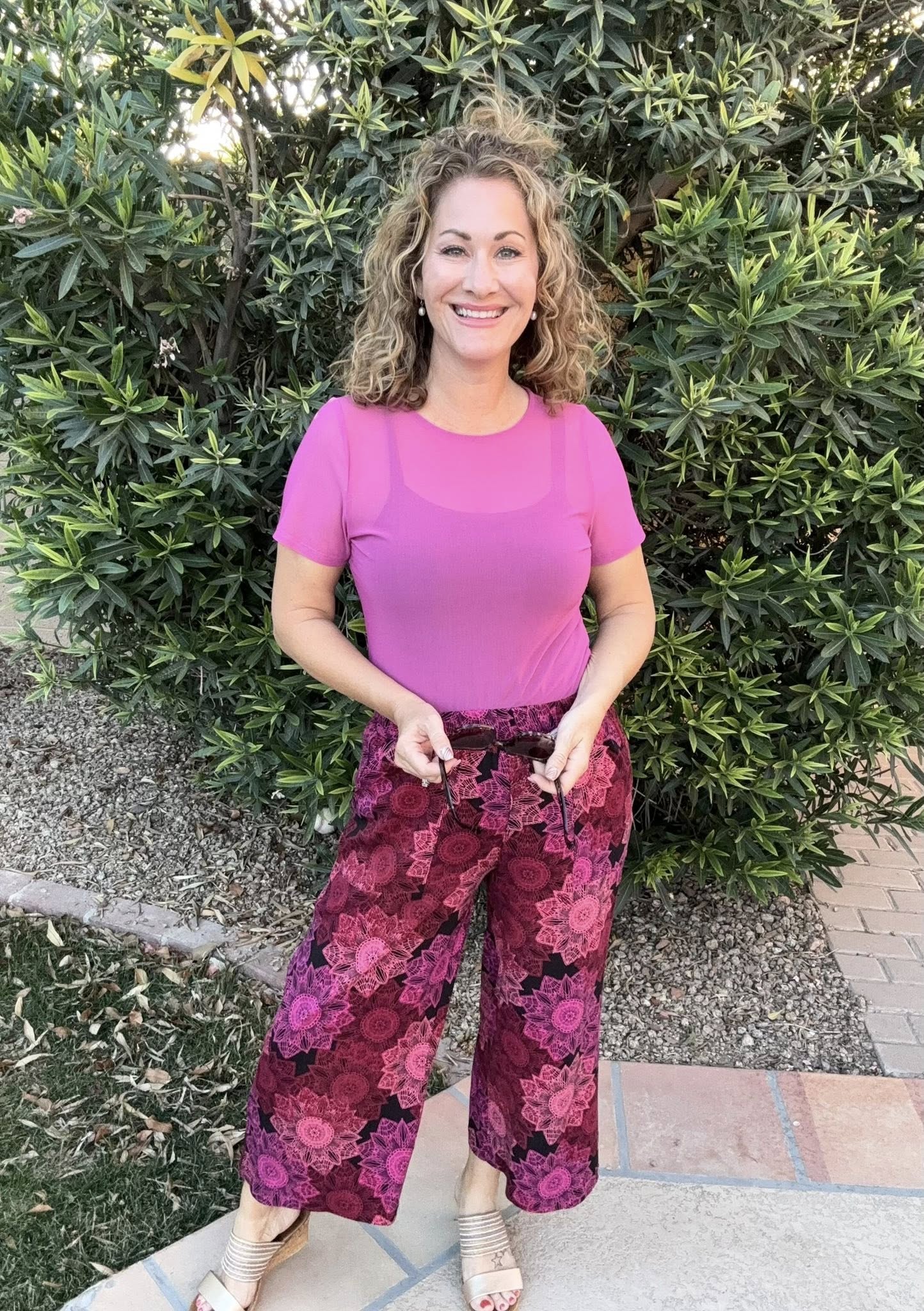 Woman wearing a solid orchid pink LuLaRoe Miranda Mesh T semi-sheer layering top outdoors with patterned pink wide leg pants, featuring lightweight mesh fabric, short sleeves, and a trendy feminine boutique fashion style.