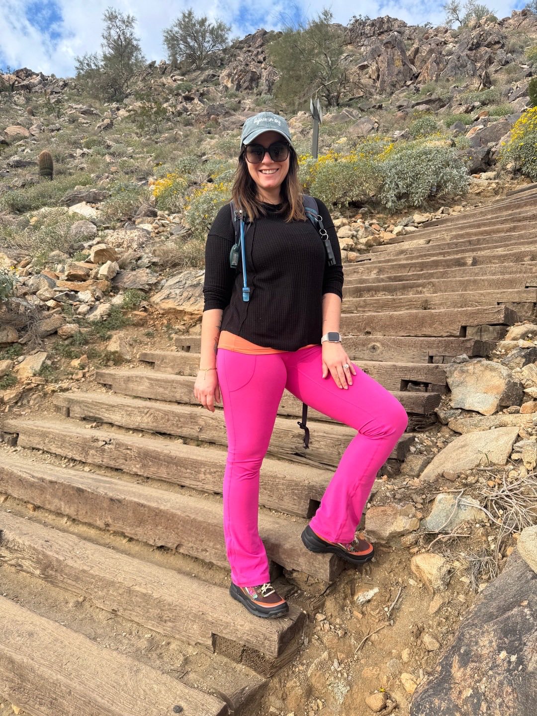 Woman in black top and LuLaRoe Passionate Yoga Pant in solid electric fuchsia with a straight-leg fit, yoga waistband, side hip pocket, and smooth stretch fabric standing on wooden steps in a desert landscape