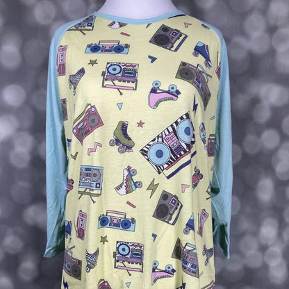 LuLaRoe Randy Tee with yellow retro print body and light aqua raglan sleeves on a mannequin against a blurred background