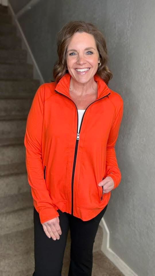 Woman wearing LuLaRoe Rise Bold jacket solid grenadine red athletic zip jacket with black zipper and pockets standing on a staircase.