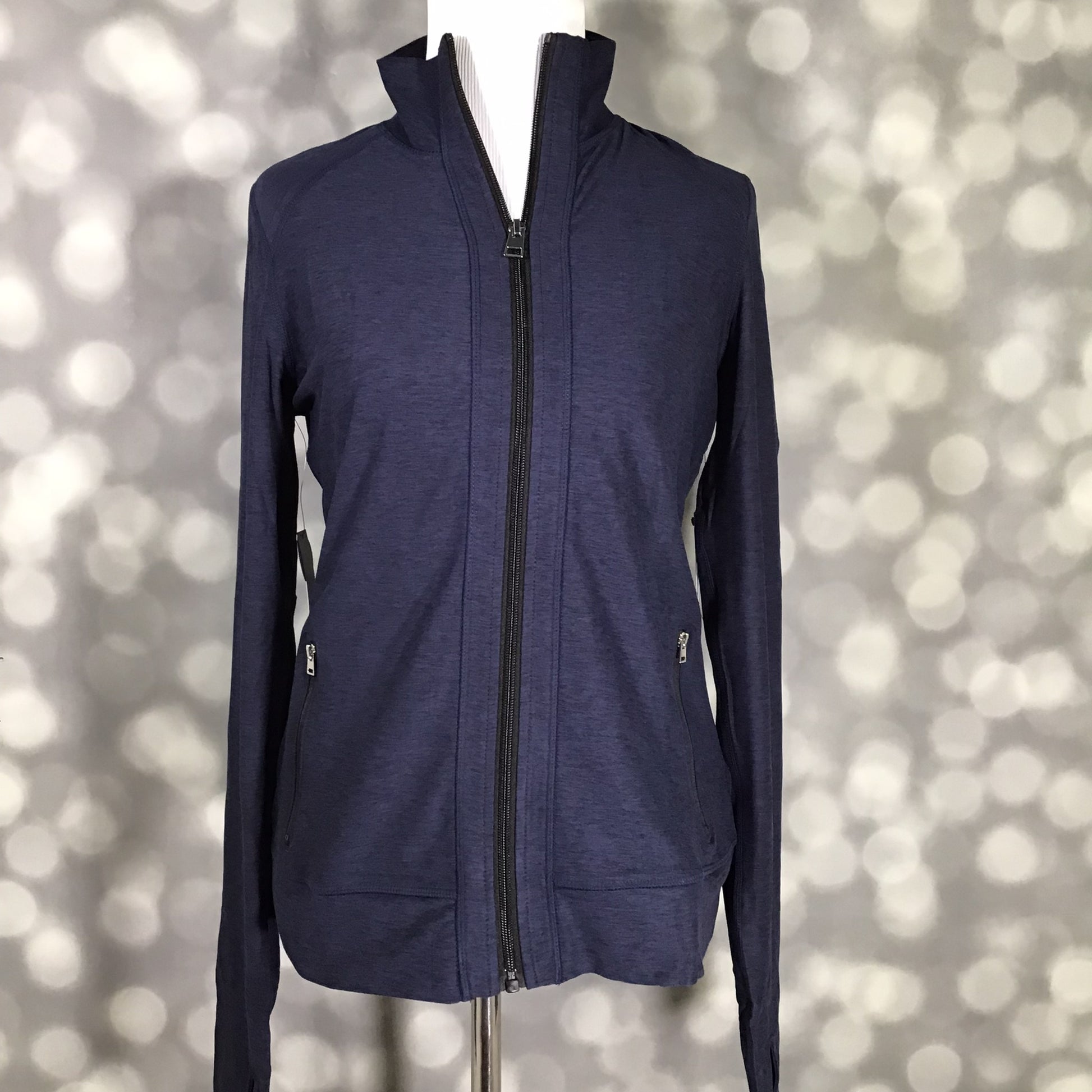 LuLaRoe Rise Bold Jacket in solid midnight navy blue displayed on a mannequin with a full zip front, high collar, long sleeves, and zippered pockets against a gray bokeh background. Sleek athletic performance jacket with a fitted silhouette perfect for layering, travel, workouts, and athleisure styling. 