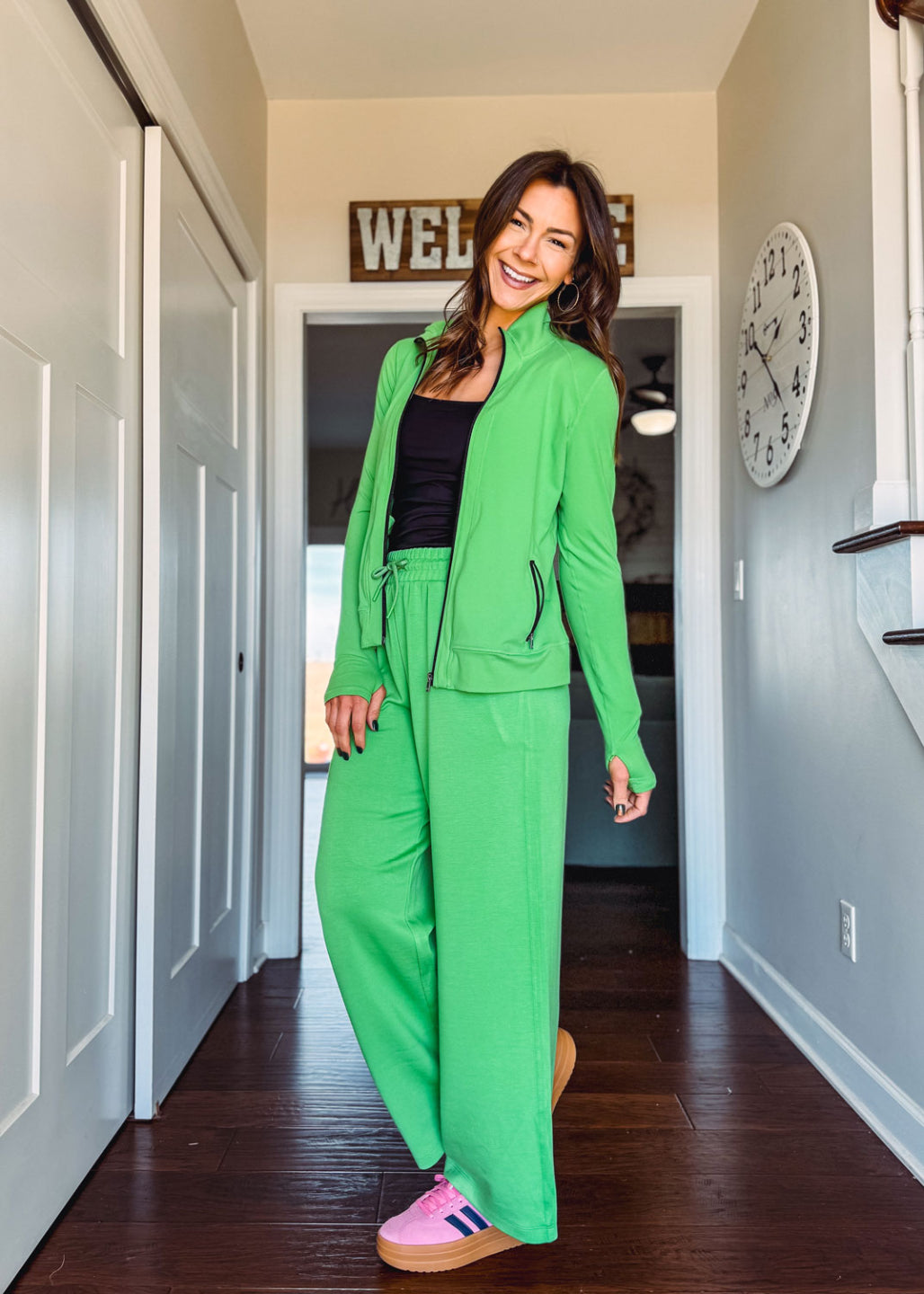 Woman in LuLaRoe Rise Bold jacket solid vibrant clover green athletic zip jacket with black zipper and pockets standing in a hallway