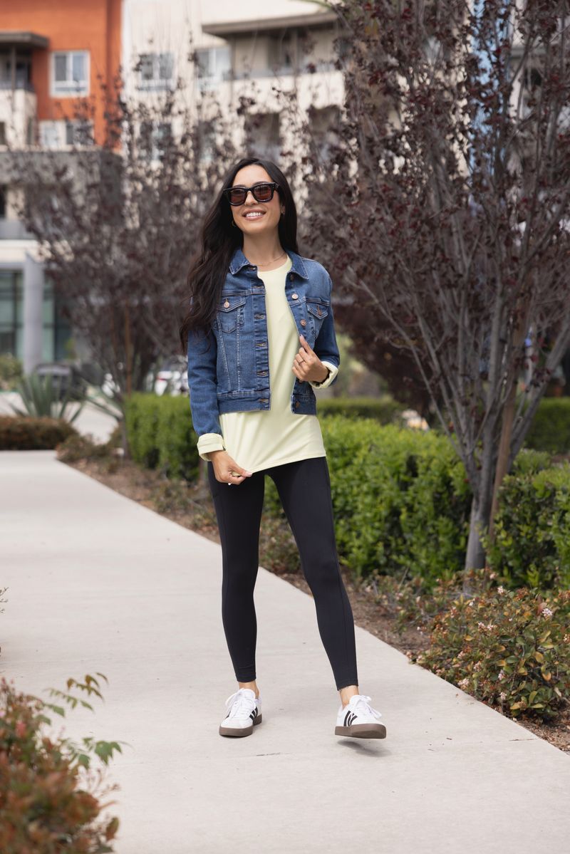 Woman wearing LuLaRoe Rise Brave solid black leggings styled with denim jacket and black leggings standing on a sidewalk.