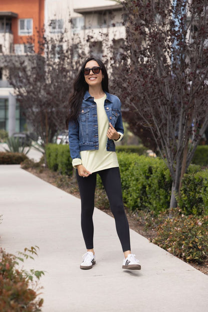 Woman wearing LuLaRoe Rise Brave solid black leggings styled with denim jacket and black leggings standing on a sidewalk.