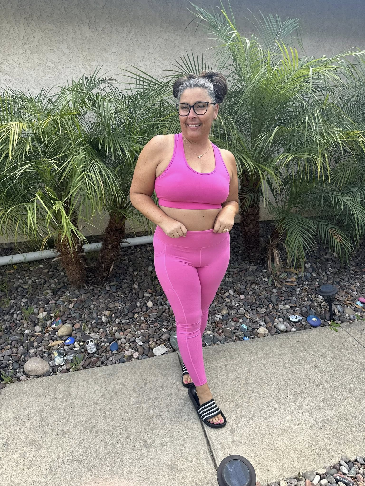 Woman wearing LuLaRoe Rise Brave leggings and sports bra in solid bright bubblegum pink standing outdoors near palm trees