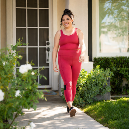Woman modeling solid berry pink LuLaRoe Rise Fearless Crop Leggings with a matching athletic tank top while walking outdoors in a sunny garden setting.
