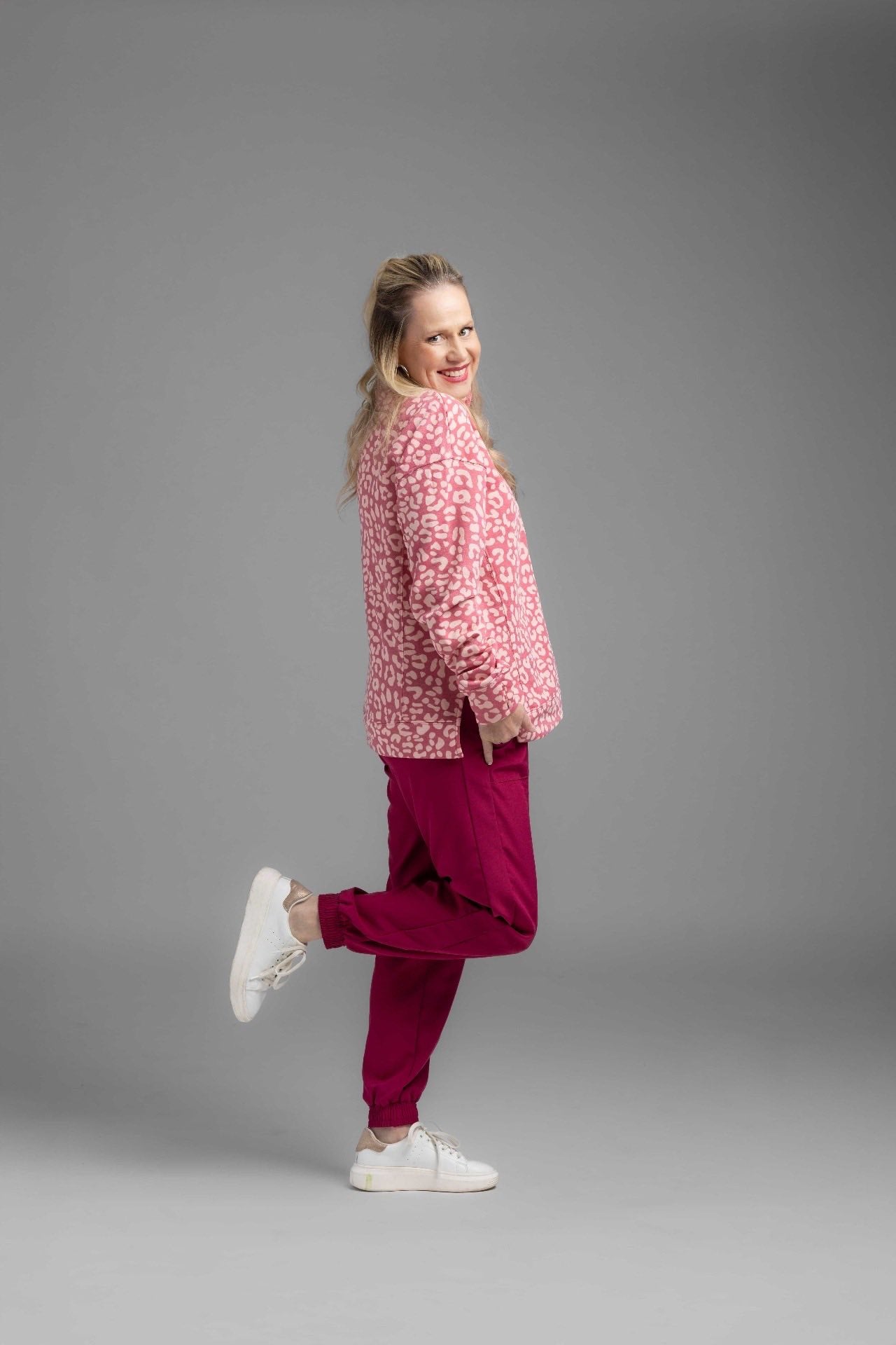 Model wearing LuLaRoe Rise Infinite Jogger in solid raspberry pink with elastic waistband and jogger cuffs, styled outdoors on red rock terrain.