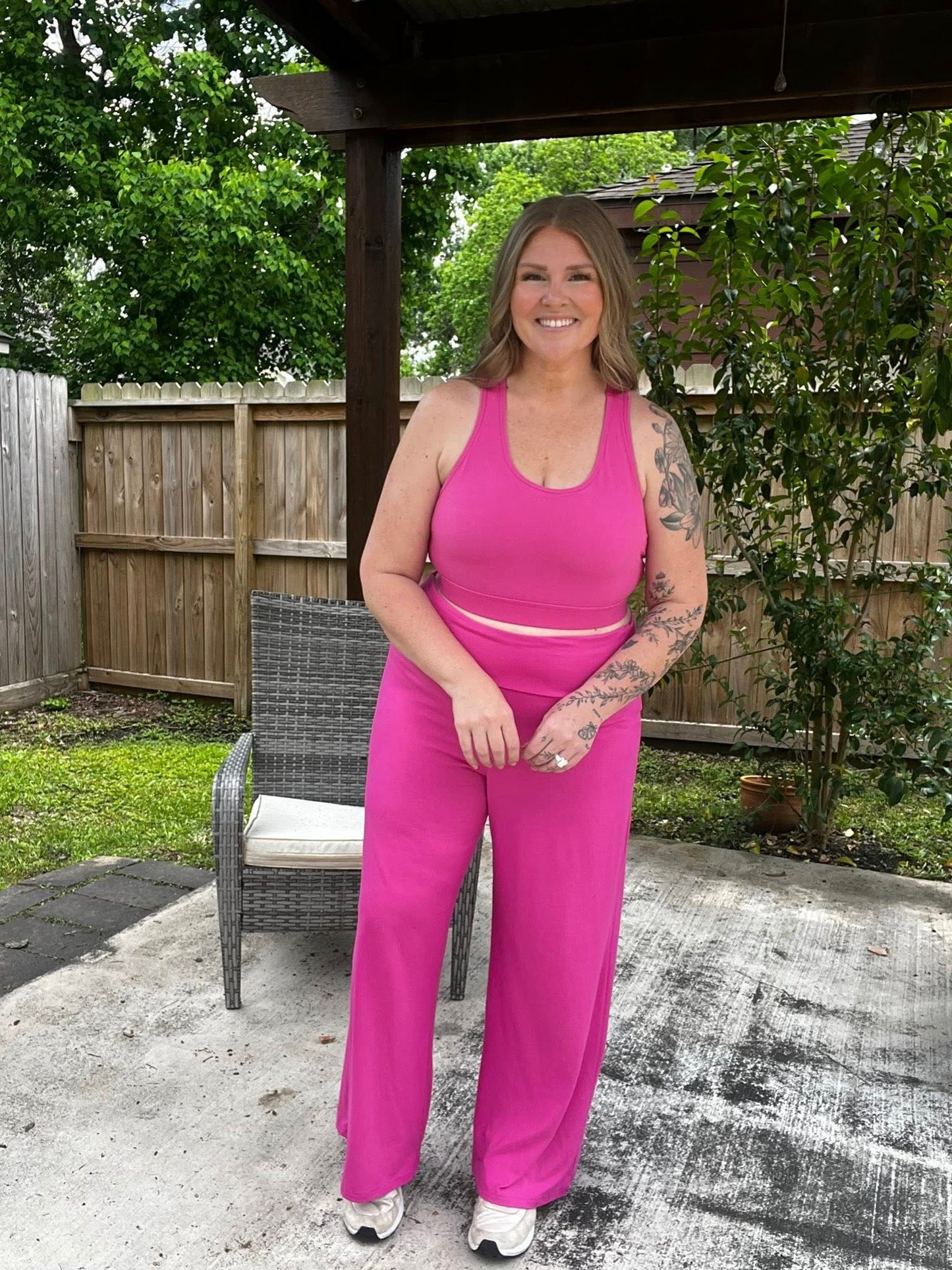Woman wearing a solid wild orchid pink LuLaRoe Rise Invincible sports bra with racerback design and matching wide leg pants, styled outdoors in a bright, bold athleisure look on a patio