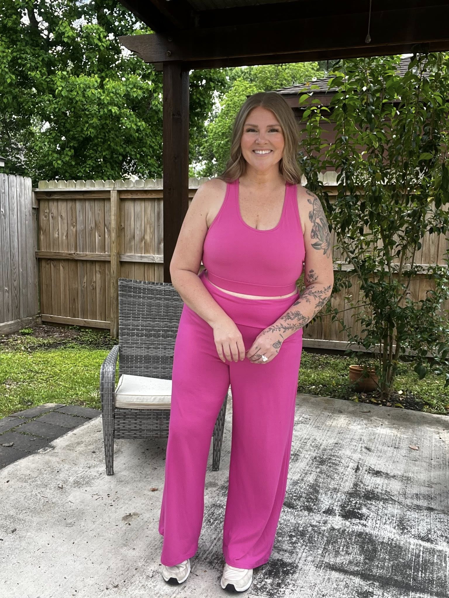 Woman wearing a solid wild orchid pink LuLaRoe Rise Invincible sports bra with racerback design and matching wide leg pants, styled outdoors in a bright, bold athleisure look on a patio
