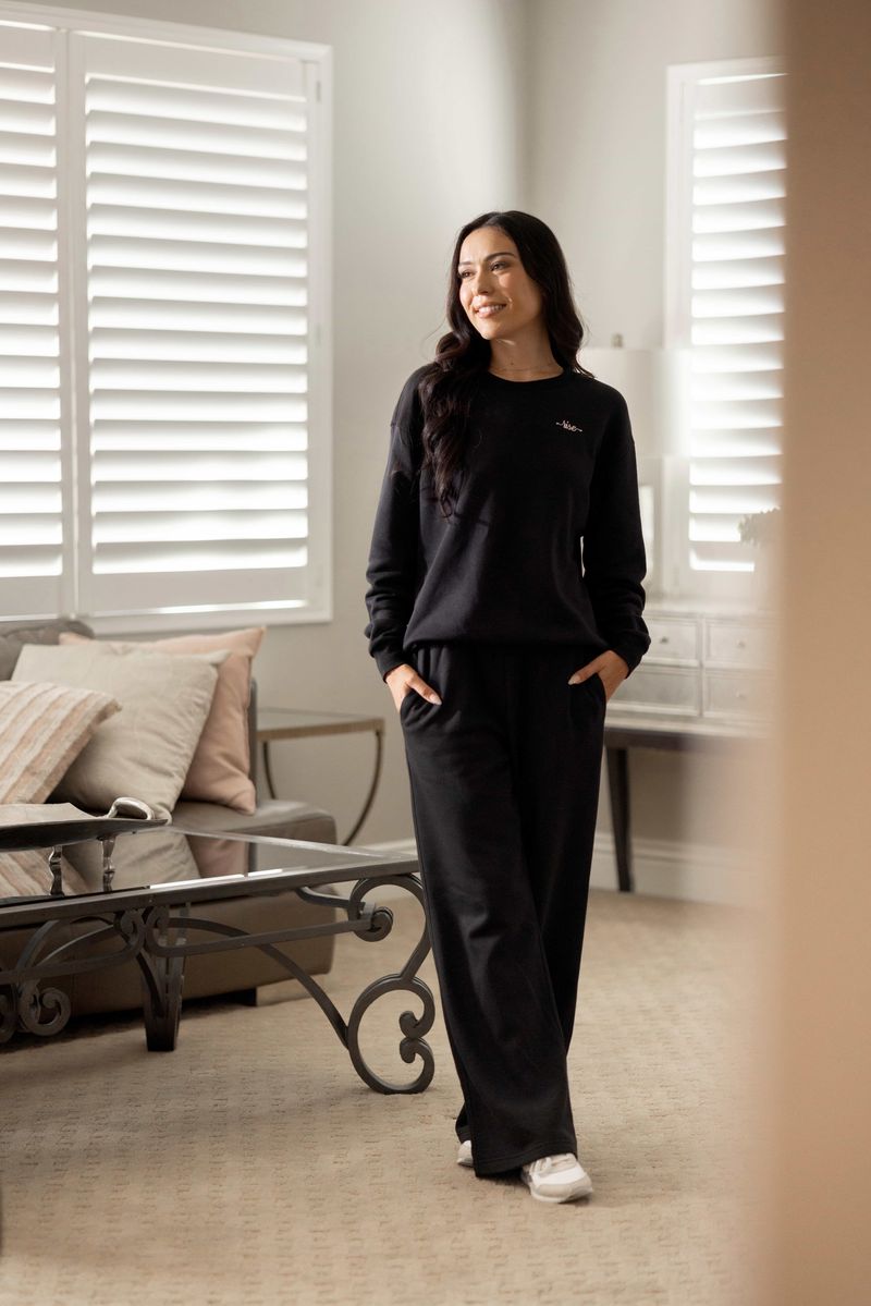 Model wearing LuLaRoe RISE Recharge Pull-On Sweatpant in solid black cotton blend fleece with relaxed wide-leg fit and elastic waistband styled for elevated loungewear.