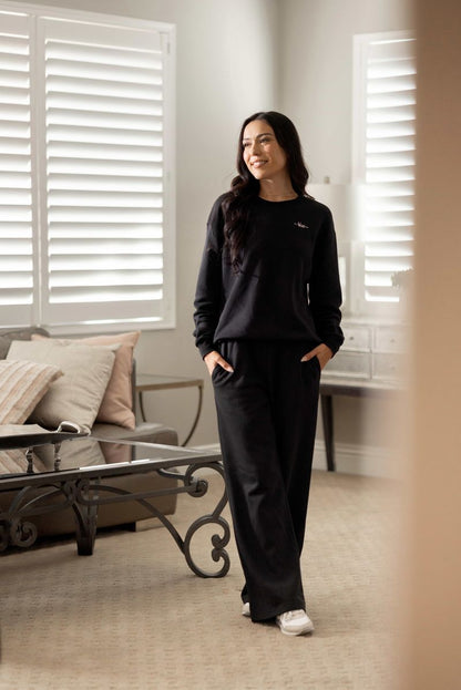 Model wearing LuLaRoe RISE Recharge Pull-On Sweatpant in solid black cotton blend fleece with relaxed wide-leg fit and elastic waistband styled for elevated loungewear.