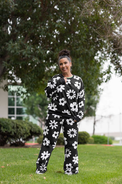 LuLaRoe RISE Reset Crew Neck Pullover in Midnight Mod Daisy featuring black fleece fabric with oversized white retro daisy print, relaxed fit with ribbed cuffs and hem with model standing outdoors with trees and grass in the background