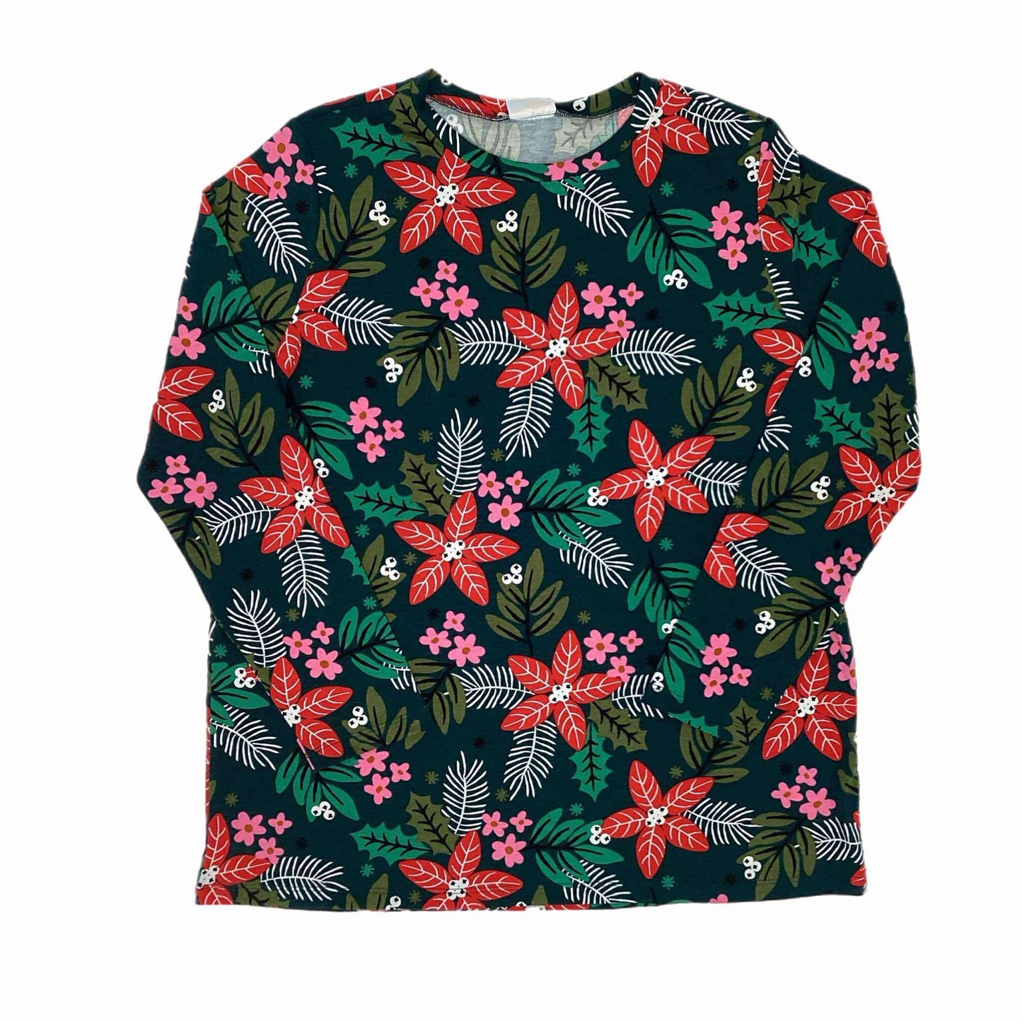 Flat lay of the LuLaRoe Sharon Top featuring a deep green background with red poinsettias, pink flowers, holly leaves, and evergreen branches. Long-sleeve tunic-length holiday floral top photographed on a white background.