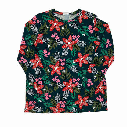 Flat lay of the LuLaRoe Sharon Top featuring a deep green background with red poinsettias, pink flowers, holly leaves, and evergreen branches. Long-sleeve tunic-length holiday floral top photographed on a white background.