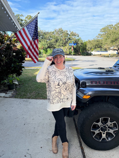 Woman wearing LuLaRoe Tammy Top with ivory base and black floral linework print, long sleeves, relaxed fit, styled with black leggings outdoors, standing in front of a truck with an American flag in the background