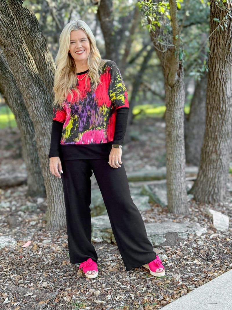 Model wearing LuLaRoe Tammy Top with colorful abstract brushstroke print and black pants with pink shoes outdoors.