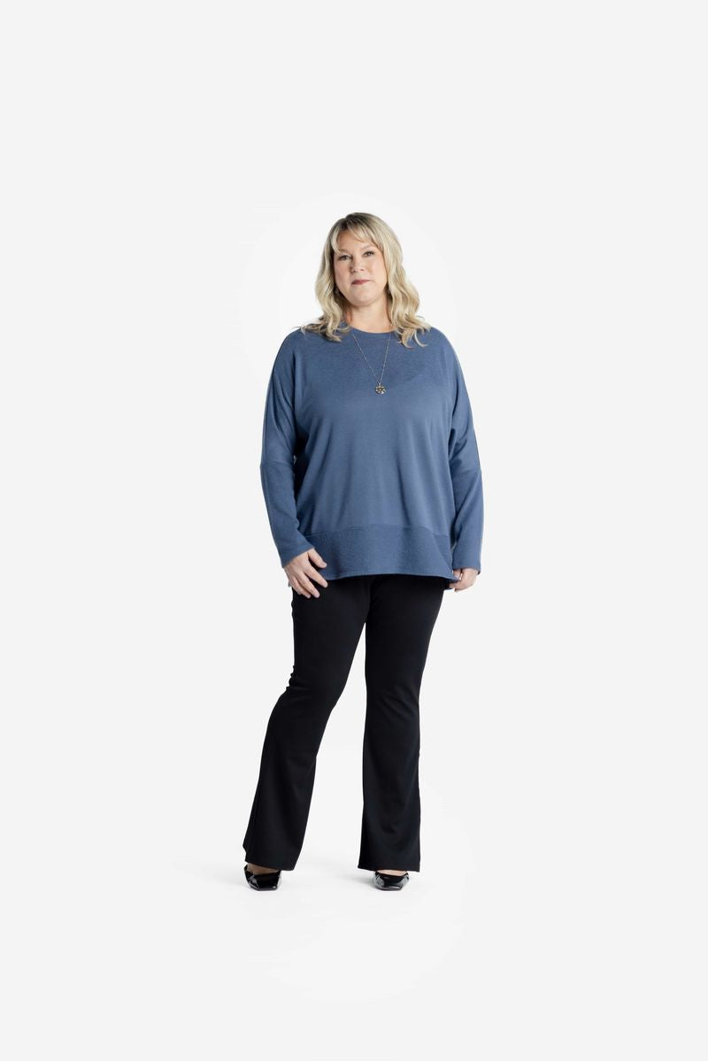 Model wearing LuLaRoe Tammy Top in solid coastal steel blue with long sleeves and relaxed fit, paired with black pants on white background