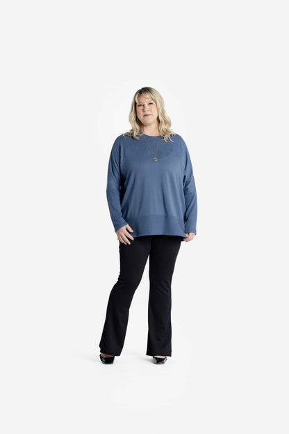 Model wearing LuLaRoe Tammy Top in solid coastal steel blue with long sleeves and relaxed fit, paired with black pants on white background