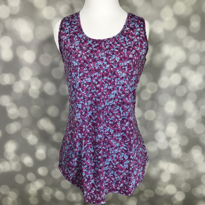 LuLaRoe tank top with berry purple background and small ditsy floral print in blue, pink, and white, featuring a scoop neckline, sleeveless design, and relaxed fit displayed on a mannequin against a blurred background