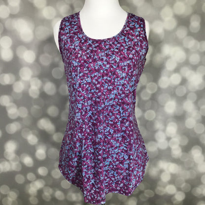 LuLaRoe tank top with berry purple background and small ditsy floral print in blue, pink, and white, featuring a scoop neckline, sleeveless design, and relaxed fit displayed on a mannequin against a blurred background