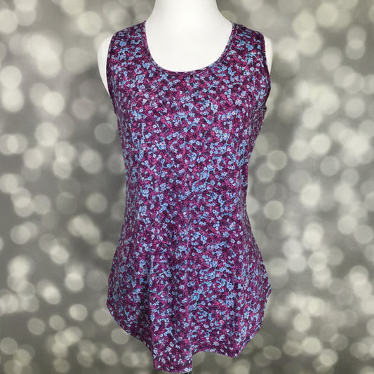 LuLaRoe tank top with berry purple background and small ditsy floral print in blue, pink, and white, featuring a scoop neckline, sleeveless design, and relaxed fit displayed on a mannequin against a blurred background