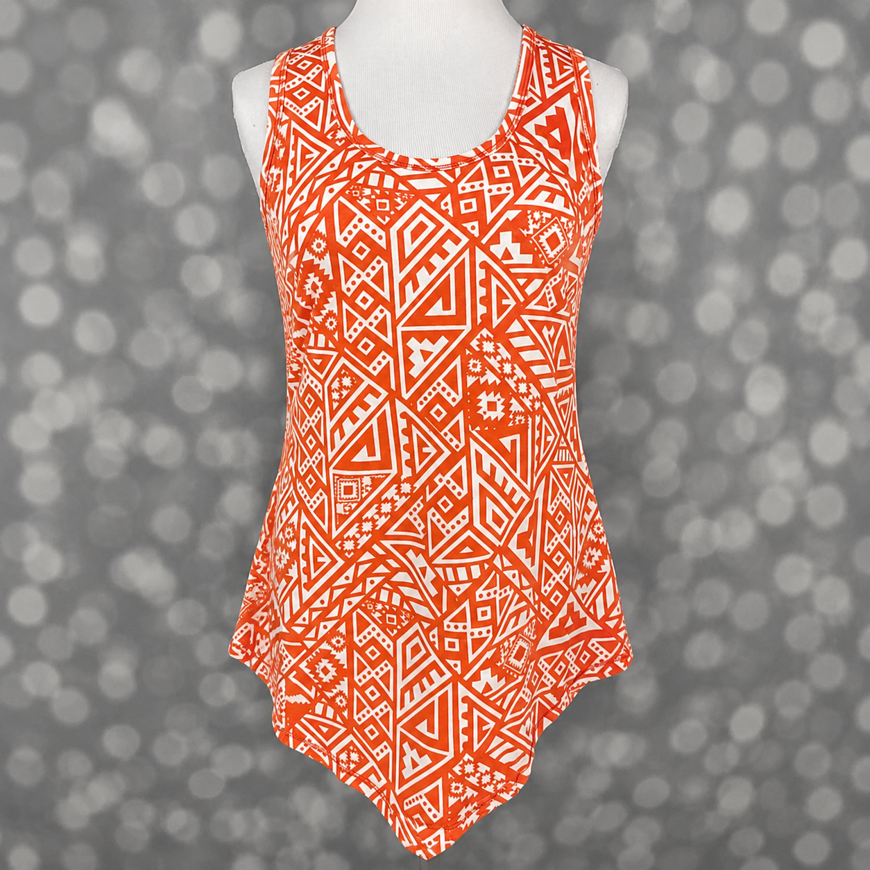 LuLaRoe tank top in Tangerine Tribal Mosaic featuring a vibrant orange and white geometric tribal pattern with southwestern-inspired motifs, sleeveless design, scoop neckline, and relaxed fit on a mannequin against a gray background. Women's boutique tank top perfect for summer outfits, vacation wear, and casual everyday styling.