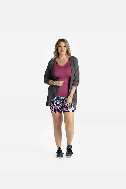 Model wearing LuLaRoe Tracy cocoon cardigan in charcoal gray layered over a pink tank and patterned biker shorts, featuring a relaxed draped fit and lightweight ribbed texture styled with sneakers on a white background