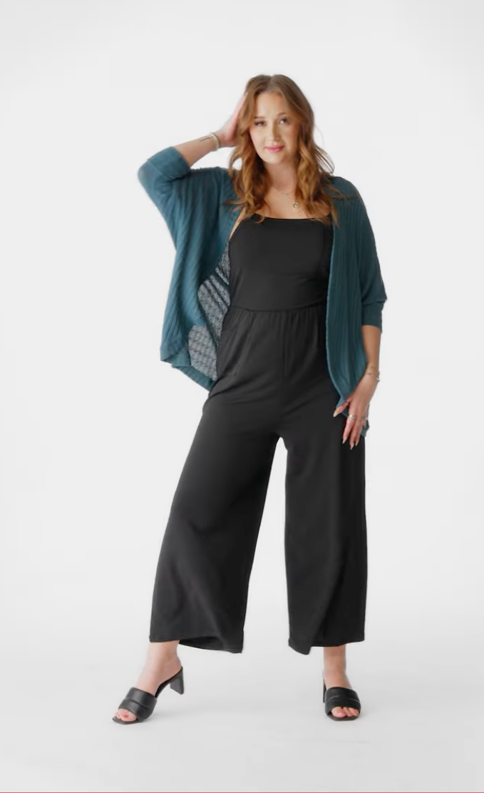 Model wearing LuLaRoe Tracy cocoon cardigan in deep teal layered over a black jumpsuit, featuring a relaxed draped fit and lightweight ribbed texture styled with black heels on a neutral background