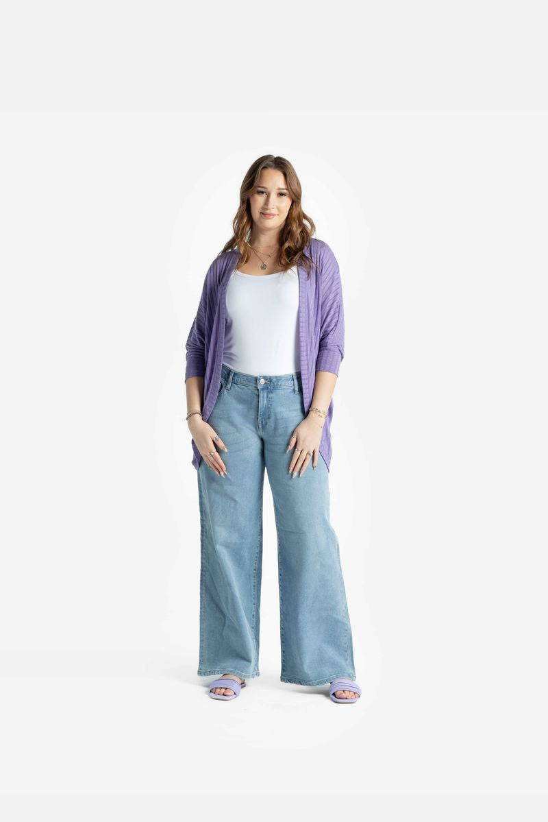 Model wearing LuLaRoe Tracy cocoon cardigan in soft lavender purple layered over a light tank and wide leg denim jeans, featuring a relaxed draped fit and lightweight ribbed texture on a white background
