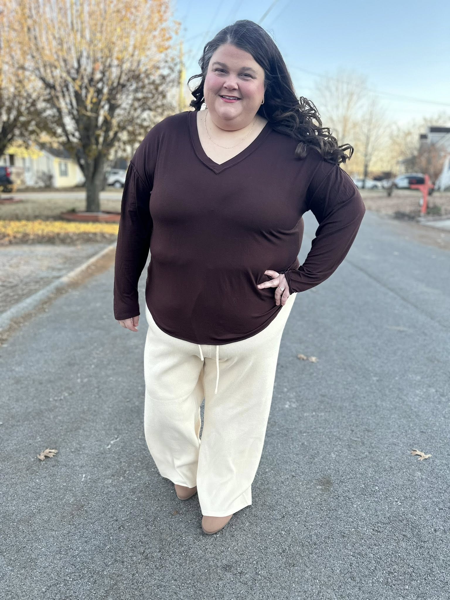 Woman wearing a LuLaRoe Vicki Top in solid chocolate brown with a raw-edge V-neck and long sleeves, styled outdoors on a residential street.
