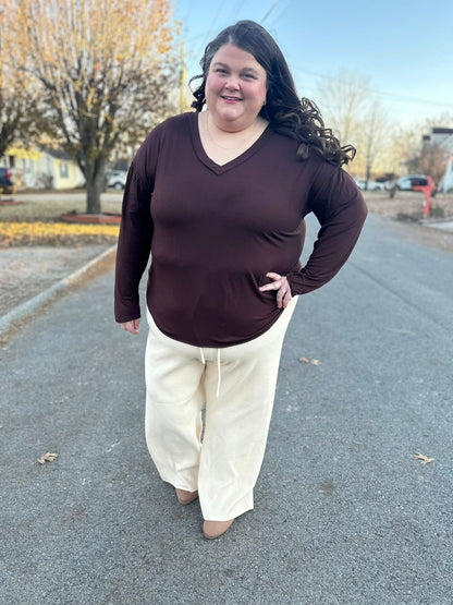 Woman wearing a LuLaRoe Vicki Top in solid chocolate brown with a raw-edge V-neck and long sleeves, styled outdoors on a residential street.