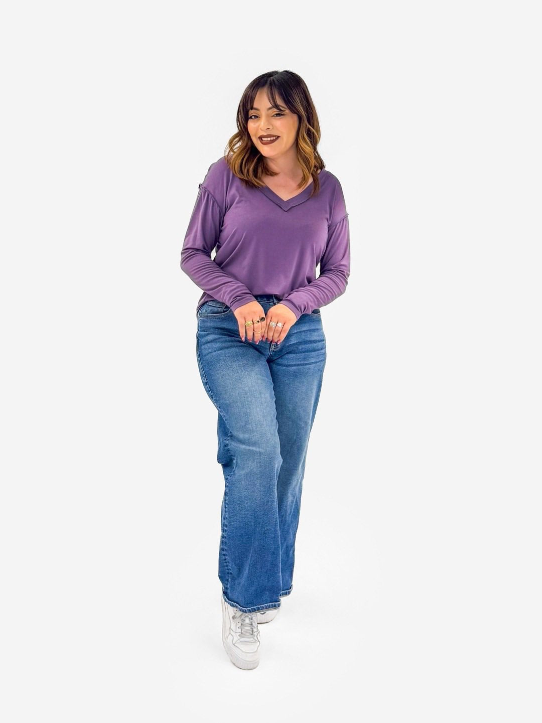 Woman wearing a LuLaRoe Vicki Top in solid soft grape purple with a raw-edge V-neck, long sleeves, and relaxed fit on a white background.