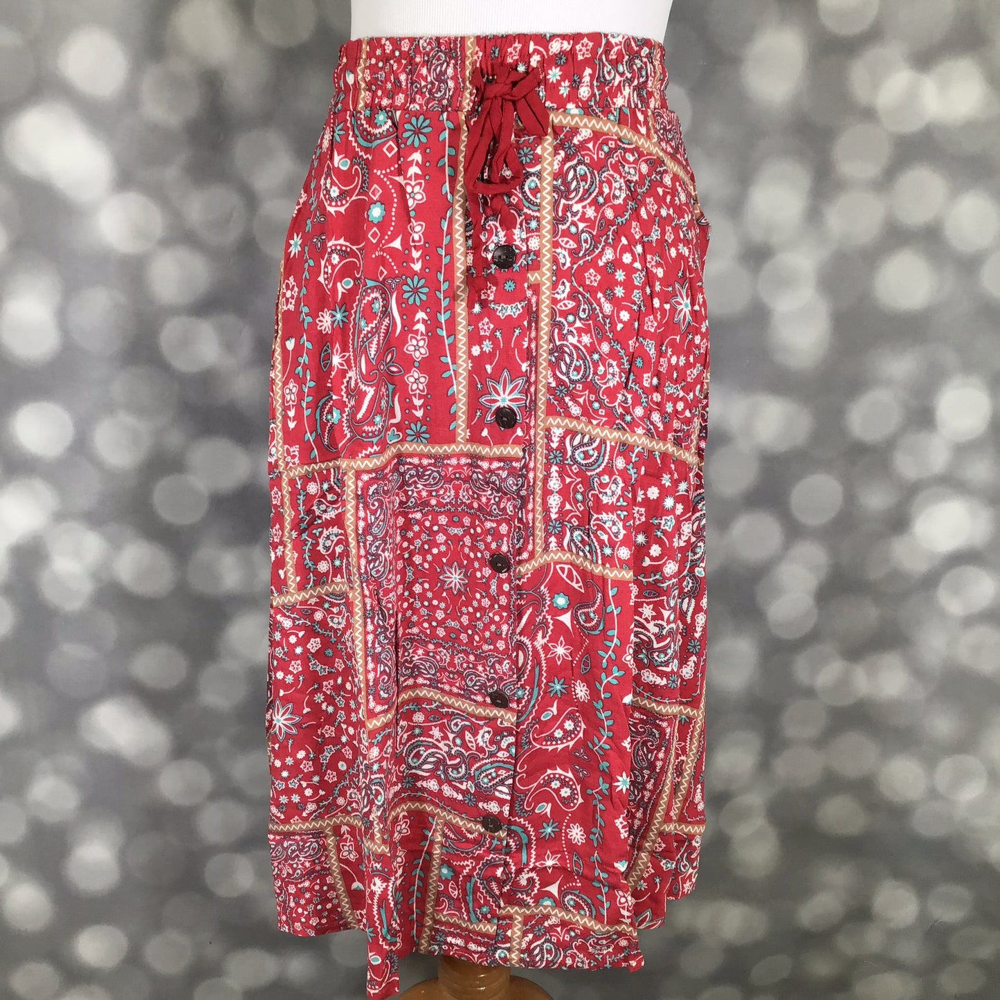 LuLaRoe Marsha Skirt with button-front detail featuring a red patchwork paisley print with elastic waistband and drawstring tie on a mannequin against a blurred gray background