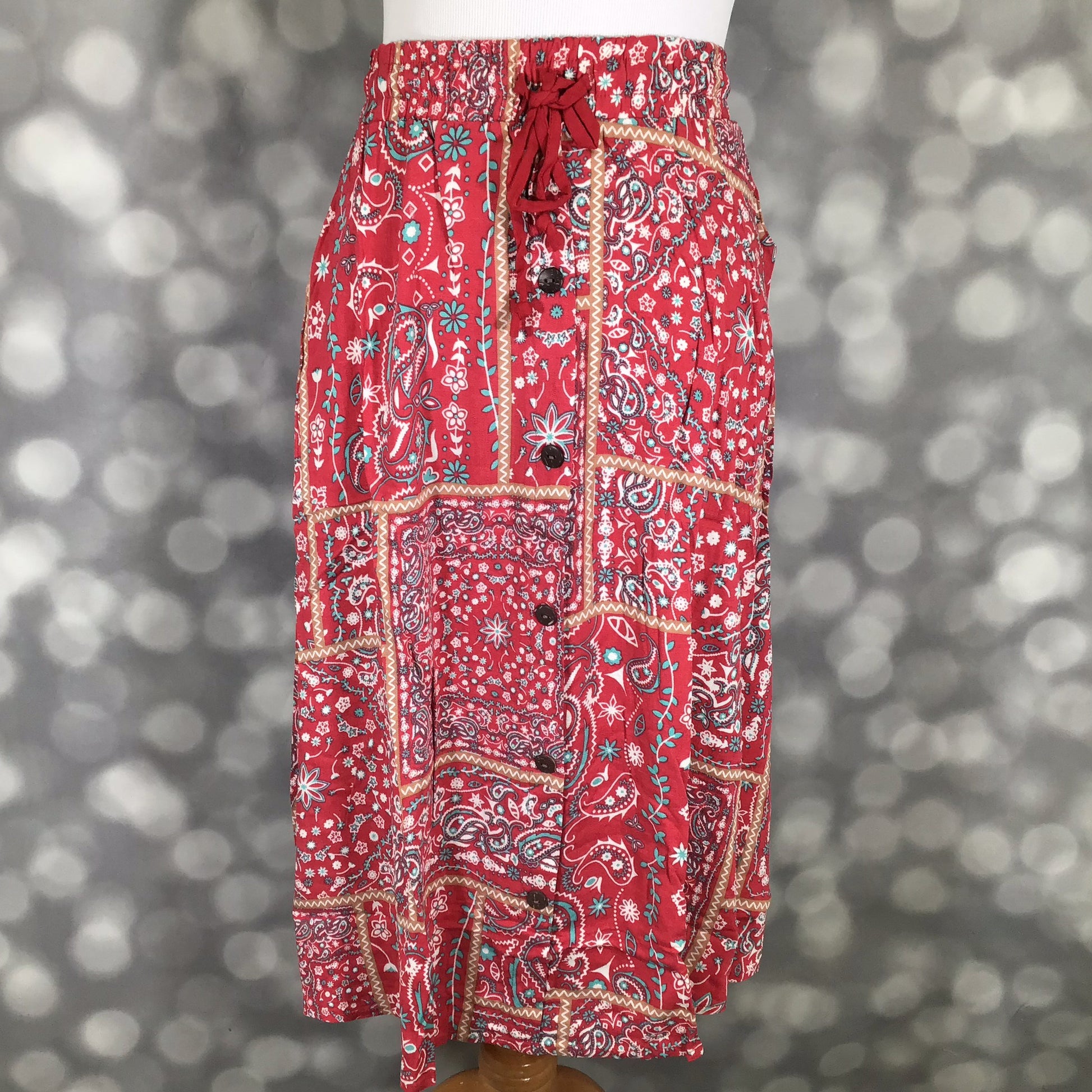 LuLaRoe Marsha Skirt with button-front detail featuring a red patchwork paisley print with elastic waistband and drawstring tie on a mannequin against a blurred gray background