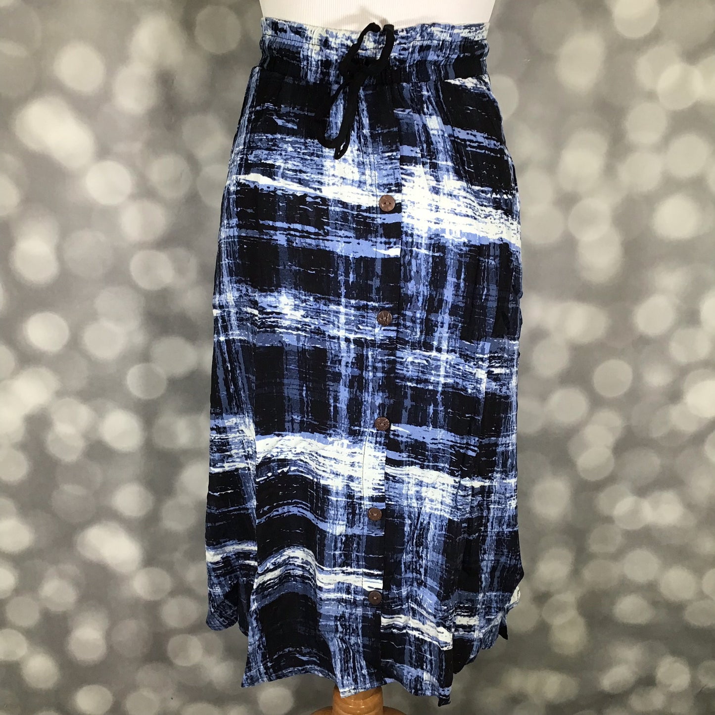 LuLaRoe Marsha Skirt with button-front detail featuring a black and blue abstract crosshatch print with elastic waistband and drawstring tie on a mannequin against a blurred background