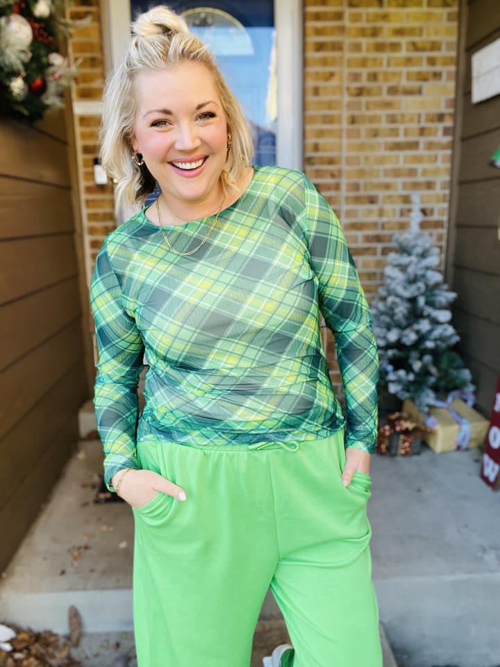 Woman wearing a LuLaRoe May long sleeve mesh top in green plaid with lime and yellow accents, fitted silhouette, semi-sheer mesh fabric, styled casually outdoors