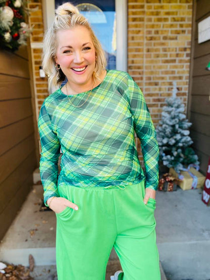 Woman wearing a LuLaRoe May long sleeve mesh top in green plaid with lime and yellow accents, fitted silhouette, semi-sheer mesh fabric, styled casually outdoors