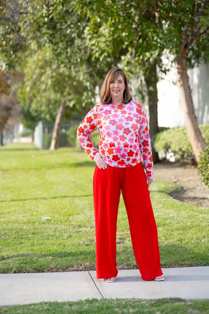 Woman wearing a LuLaRoe May long sleeve mesh top in white with red and coral floral print, fitted silhouette, lightweight semi-sheer mesh fabric styled outdoors with red pants