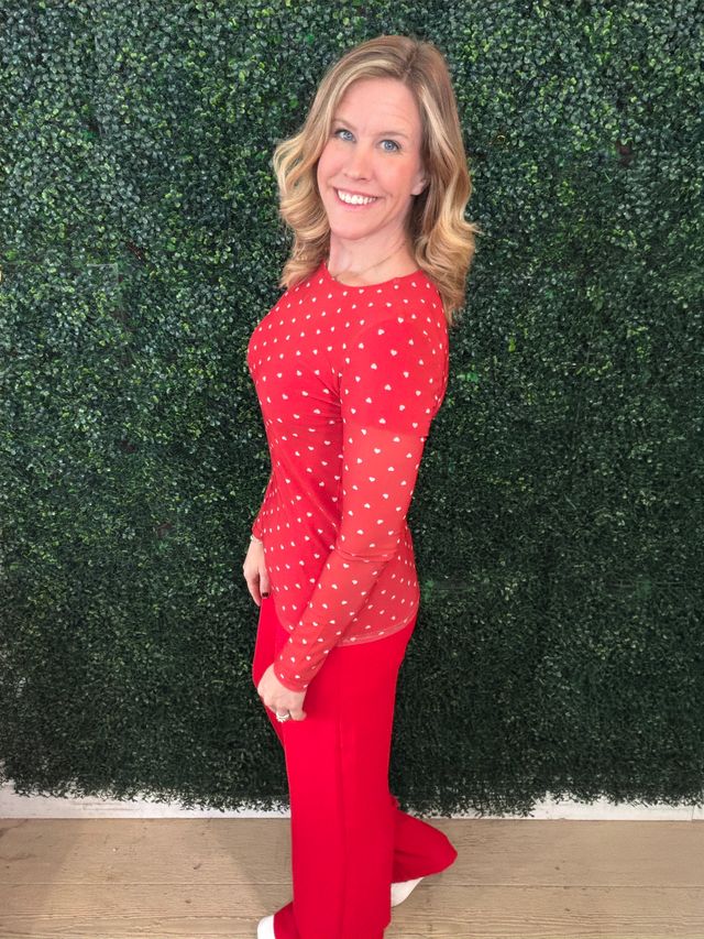 Woman wearing a LuLaRoe May long sleeve mesh top in bright red with small white heart print, fitted silhouette, lightweight semi-sheer mesh fabric styled casually