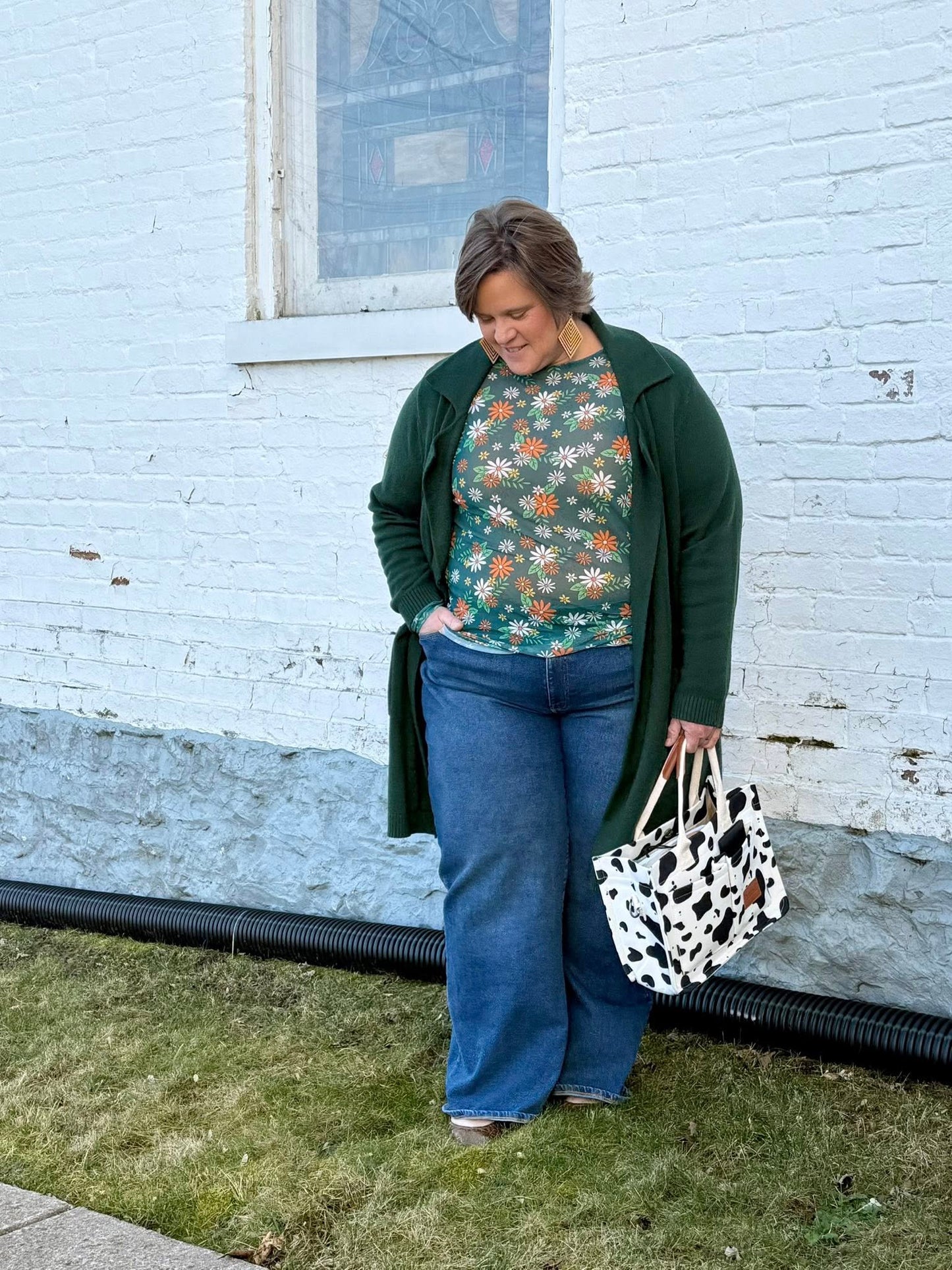 Woman wearing a LuLaRoe May long sleeve mesh top in green with scattered daisy floral print, fitted silhouette, lightweight semi-sheer mesh fabric styled casually with denim and a cardigan