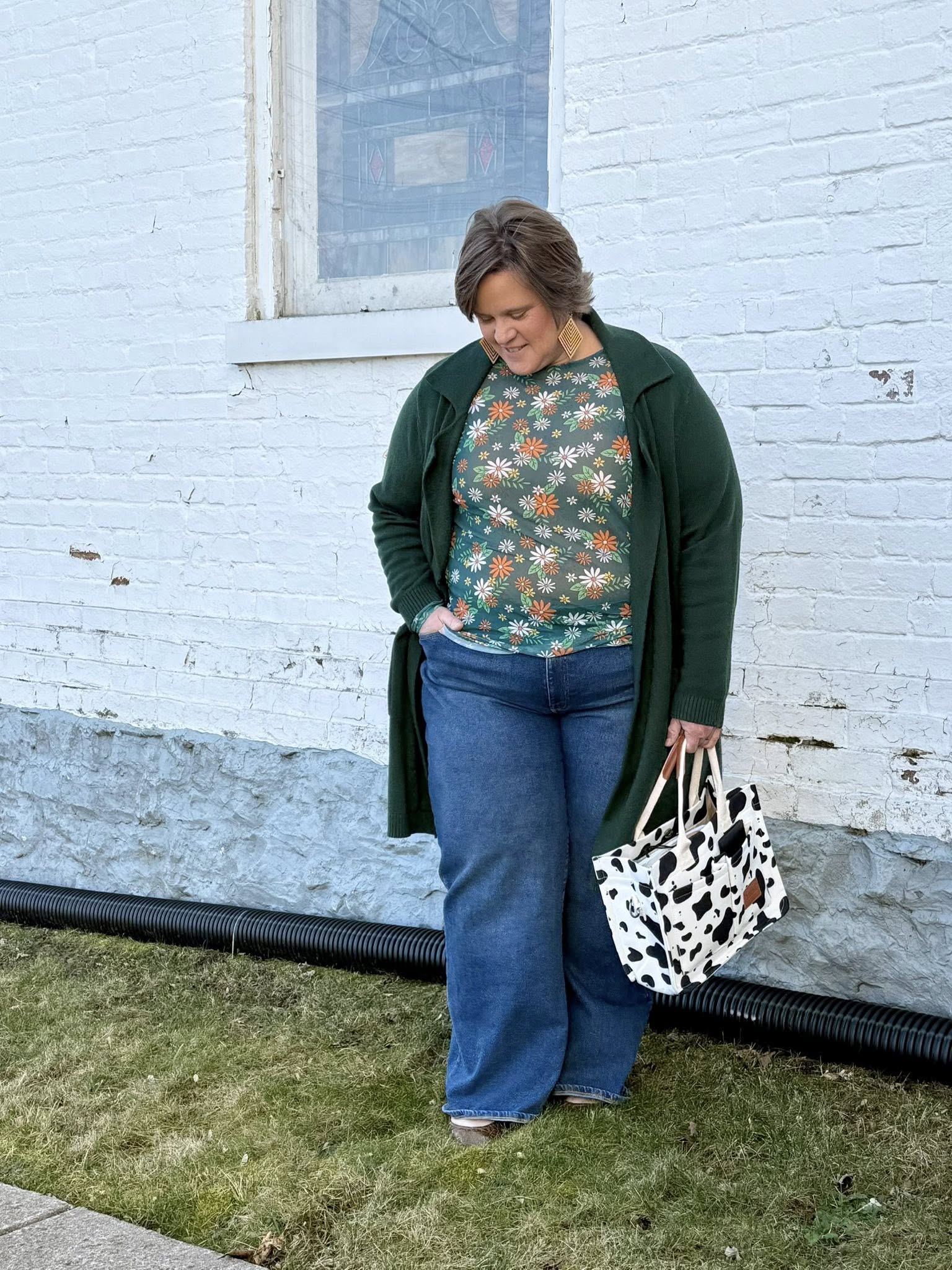 Woman wearing a LuLaRoe May long sleeve mesh top in green with scattered daisy floral print, fitted silhouette, lightweight semi-sheer mesh fabric styled casually with denim and a cardigan